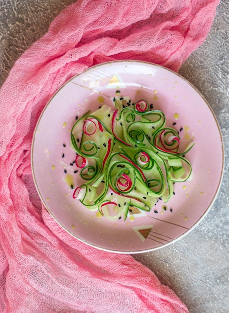 A top-down view of a colorful salad bowl filled with prebiotic-rich foods like asparagus, onions, garlic, bananas, and oats. The bowl is placed on a rustic wooden table, surrounded by scattered fresh herbs.