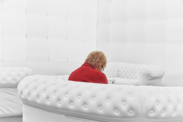 A brightly lit, modern hospital waiting room with several empty chairs. An elderly woman sits alone, looking anxiously at the clock on the wall. The scene conveys the feeling of long wait times and the potential isolation experienced by patients due to healthcare staffing shortages.