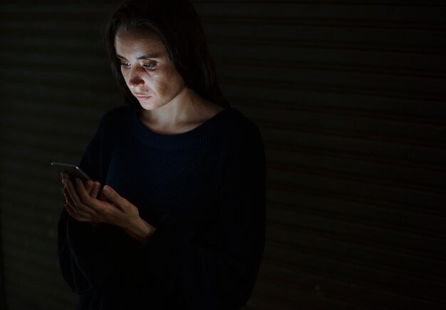 A person looking distressed at their phone, receiving a hateful message. The background is dark and blurry, symbolizing the isolating effect of cyberbullying.