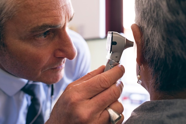 A close-up of an audiologist performing a hearing test on a senior man. The audiologist is wearing a lab coat and appears to be explaining the test results to the patient. The setting is a quiet and professional audiology clinic.