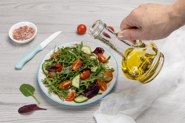 A close-up shot of a hand pouring olive oil over a vibrant salad composed of mixed greens, tomatoes, cucumbers, olives, feta cheese, and a sprinkle of herbs. The texture and colors of the fresh ingredients are emphasized, showcasing the healthy and appetizing nature of the salad.