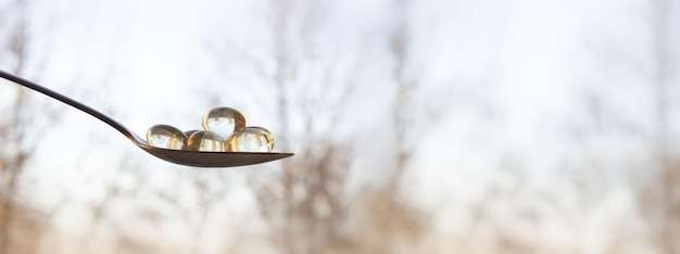 A close-up of vitamin D capsules being poured onto a spoon, with a sunny landscape in the background, emphasizing the connection between sunlight and vitamin D production.