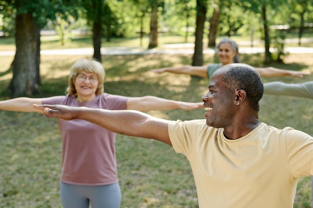 A diverse group of seniors participates in a Tai Chi class outdoors in a park. They move slowly and deliberately, following the instructor's lead.