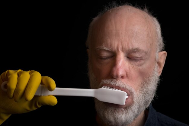 An older man with arthritis struggles to hold a toothbrush due to joint pain. The image highlights the challenges some seniors face with maintaining proper oral hygiene.
