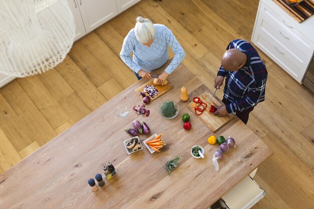 An overhead shot of a senior couple preparing a healthy meal together in their kitchen. They are surrounded by fresh vegetables and fruits, with a cookbook open on the counter.