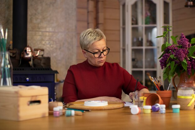 An older woman smiling and concentrating while working on a Sudoku puzzle in a sunlit room, showcasing cognitive stimulation.