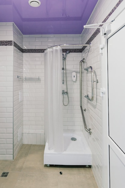 A modern bathroom equipped with multiple grab bars, a walk-in shower with a built-in seat, and non-slip flooring. The lighting is bright and even.