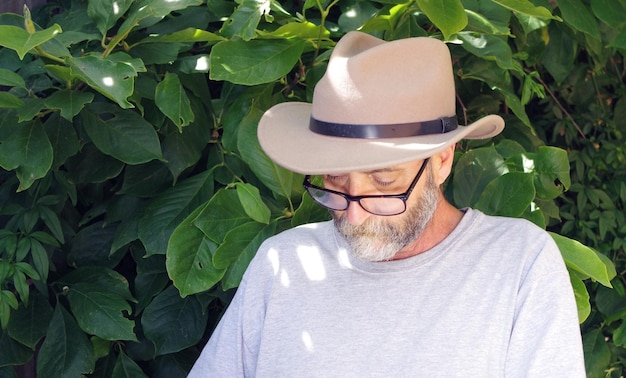 A senior man wearing a wide-brimmed hat, sunglasses, and a long-sleeved shirt while gardening, demonstrating comprehensive sun protection through clothing and accessories.