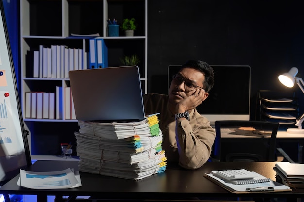 A person sitting at a desk, looking stressed and overwhelmed with multiple screens and stacks of papers surrounding them. The lighting is dim, emphasizing the feeling of pressure and anxiety. The image captures the intensity of a stressful work environment.