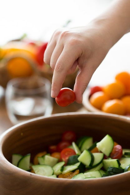 A close-up shot of a person's hands preparing a colorful salad with various fresh vegetables like tomatoes, cucumbers, lettuce, and bell peppers. The focus is on healthy eating and making nutritious food choices. The background is a blurred kitchen setting, emphasizing the importance of home-cooked meals.