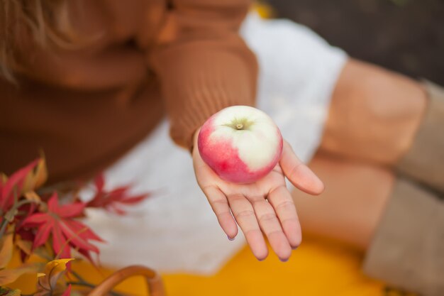 A person holding a red apple with a bite taken out of it, with a blurred background of an apple orchard during the autumn season.