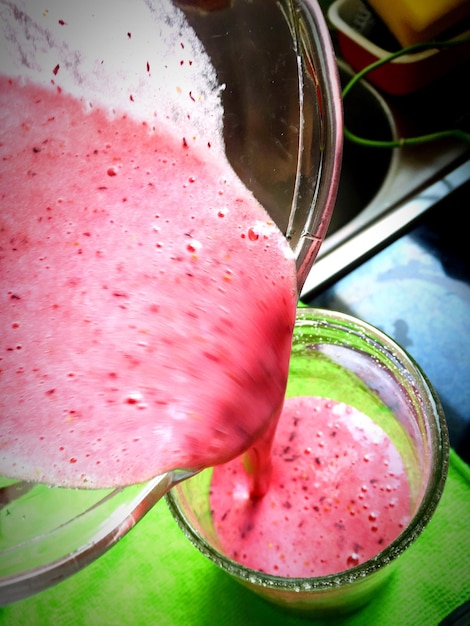 A close-up shot of a vibrant fruit smoothie being poured into a glass, with visible chunks of fruits like berries and bananas. The background includes fresh fruits displayed on a kitchen counter, indicating a healthy and refreshing start to the day.