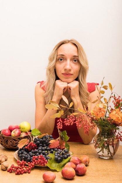 A woman looking thoughtfully at a plate with various fruits and vegetables, alongside a glass of green juice. The setting is a bright, modern kitchen, conveying a sense of mindful health decisions and lifestyle.