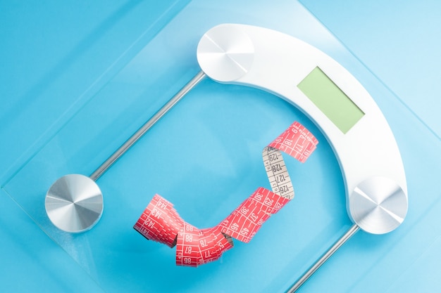 Conceptual image showing a scale with an arrow pointing downwards, a measuring tape wrapped around it, and vibrant vegetables nearby, visually representing the promise and reality of detox diets for weight loss.