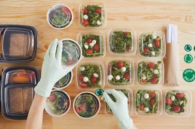 A close-up shot of hands placing pre-portioned meals into labeled containers, with various fresh ingredients such as chopped vegetables, cooked rice, and lean protein sources scattered on the countertop.