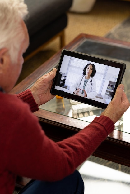 A senior patient smiling and interacting with a doctor on a tablet during a telehealth consultation, with a caregiver present in the background.