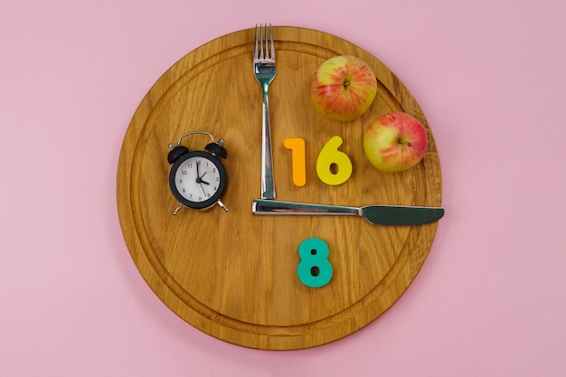 A digital clock displaying a 16:8 intermittent fasting schedule, with a graphic illustrating the eating window and fasting period. The background includes healthy food options like fruits, vegetables, and lean proteins.