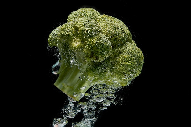 An overhead shot of a vibrant green head of broccoli, freshly washed, with droplets of water clinging to the florets, set against a dark background to emphasize the vegetable's color and texture.
