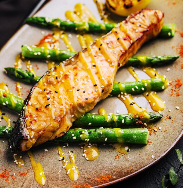 A close-up shot of a perfectly grilled salmon fillet served with a side of fresh asparagus and a lemon wedge. The salmon is glistening with natural oils, emphasizing its richness in Omega-3 fatty acids.