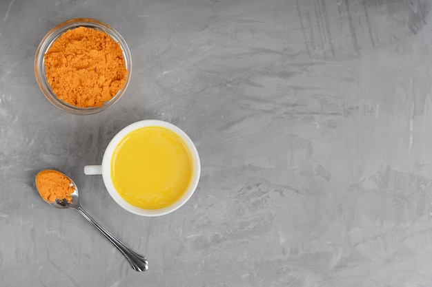 A top-down shot of a bowl filled with vibrant yellow turmeric powder, next to a fresh turmeric root sliced open to reveal its deep orange interior. The scene is softly lit to highlight the spice's rich color and texture.